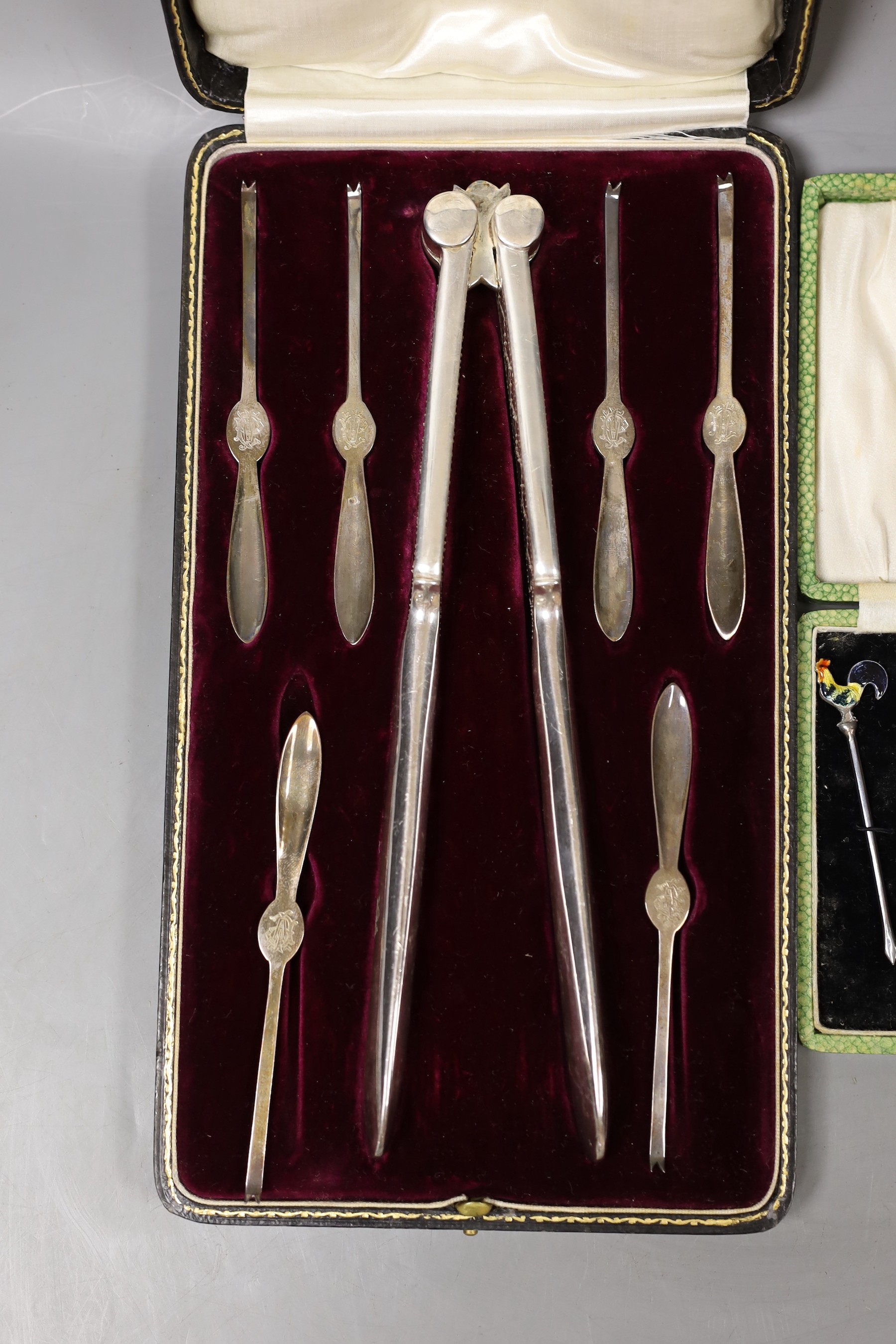 A George V cased set of six silver lobster picks and plated crackers and a similar set of silver and enamel cocktail sticks